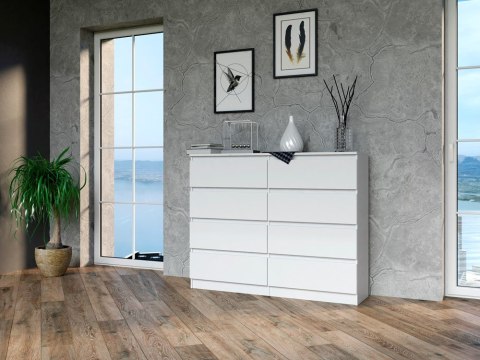 Komoda KOM-907-BIEL-MAT w aranżacji nowoczesnego salonu – widok w półprofilu na tle szarej ściany.